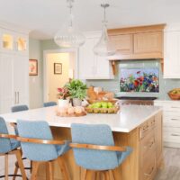 White kitchen cabinets and countertops, rift cut white oak range hood and kitchen island, color mosaic backsplash light blue fabric high-backed bar stools