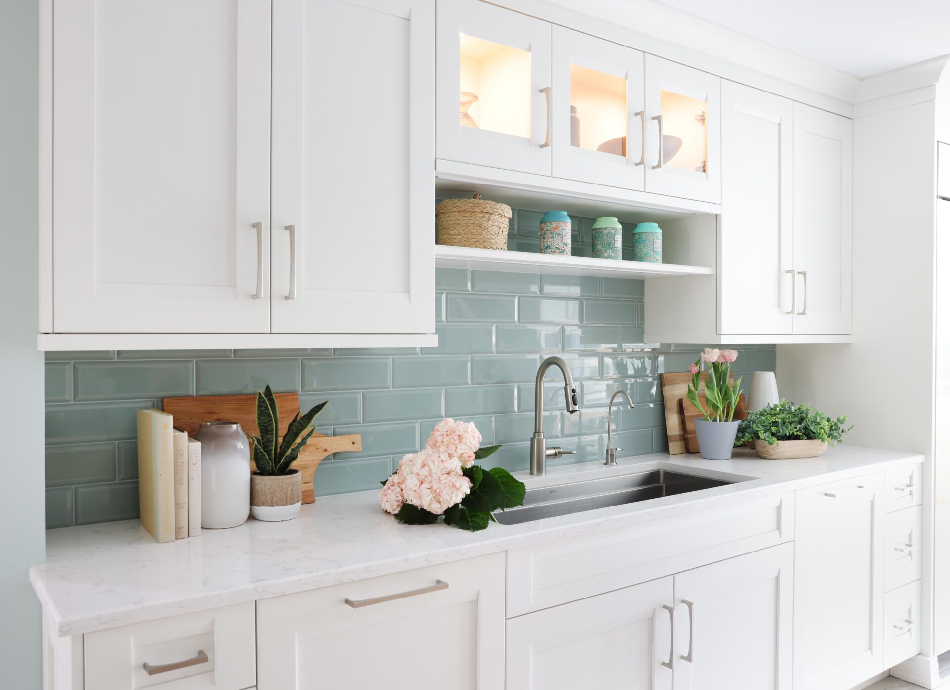 White kitchen cabinets with light green tile subway tile backsplash behind kitchen sink, color mugs on shelf above sink