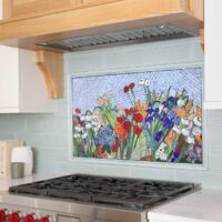 Colorful flower mosaic backsplash above range with surrounding light green subway tile, the bottom of a rift cut white oak range hood