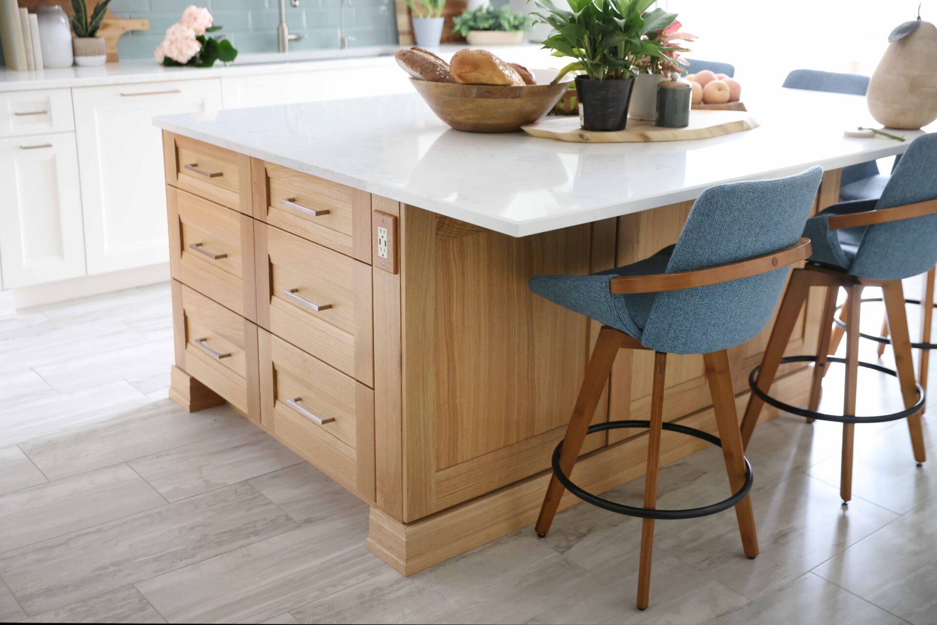 Rift cut white oak kitchen island with white countertop, gold hardware drawer pulls, wood bar stool with blue cushion