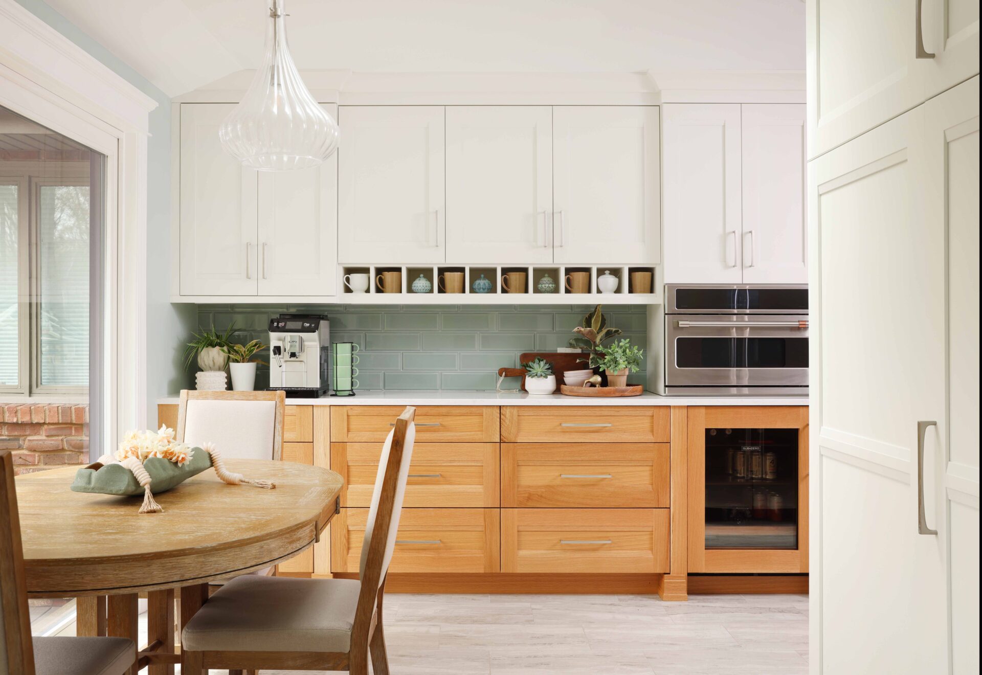 Upper white cabinets, rift cut white oak lower cabinets, coffee mugs in shelf nooks, light green tile backsplash, subway tile. cut white oak lower cabinets, coffee mugs in shelf nooks. Stainless steel microwave, below counter beverage/bar fridge refrigerator