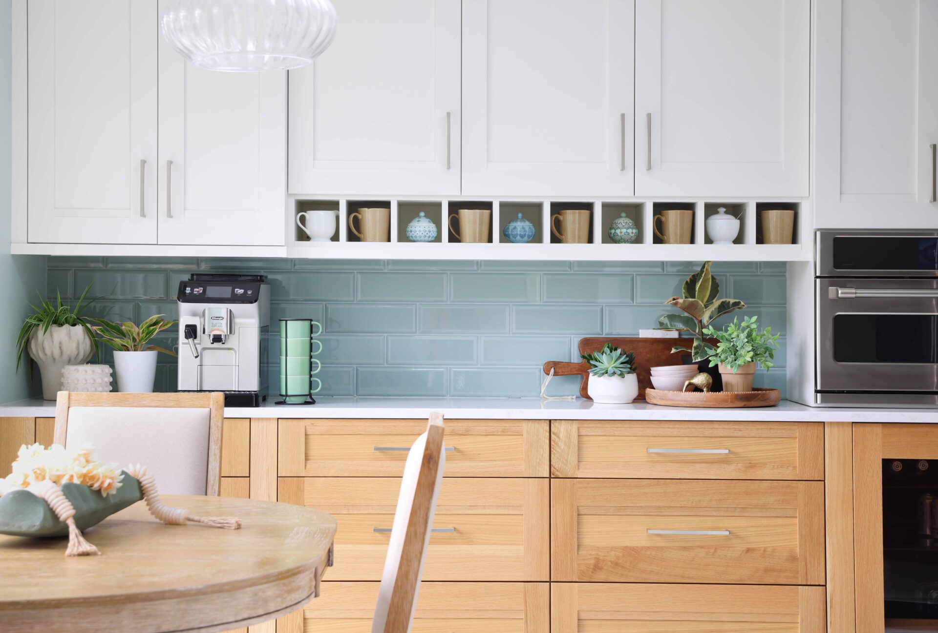 Upper white cabinets, rift cut white oak lower cabinets, coffee mugs in shelf nooks, light green tile backsplash, subway tile. cut white oak lower cabinets, coffee mugs in shelf nooks. Espresso machine on the left on counter
