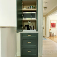 Freestanding appliance garage cabinetry in forest green, door open showing a microwave and other appliances