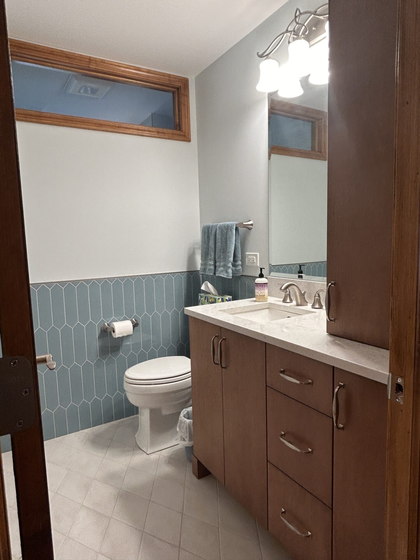 Bathroom with light blue wall tile, maple cabinetry, wood-trimmed transom window