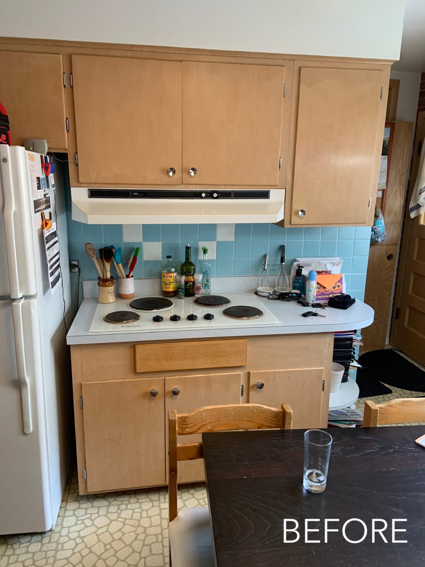 "Before" kitchen photo showing birch cabinets, white vintage rangetop, blue and white square backsplash, white fridge to the left