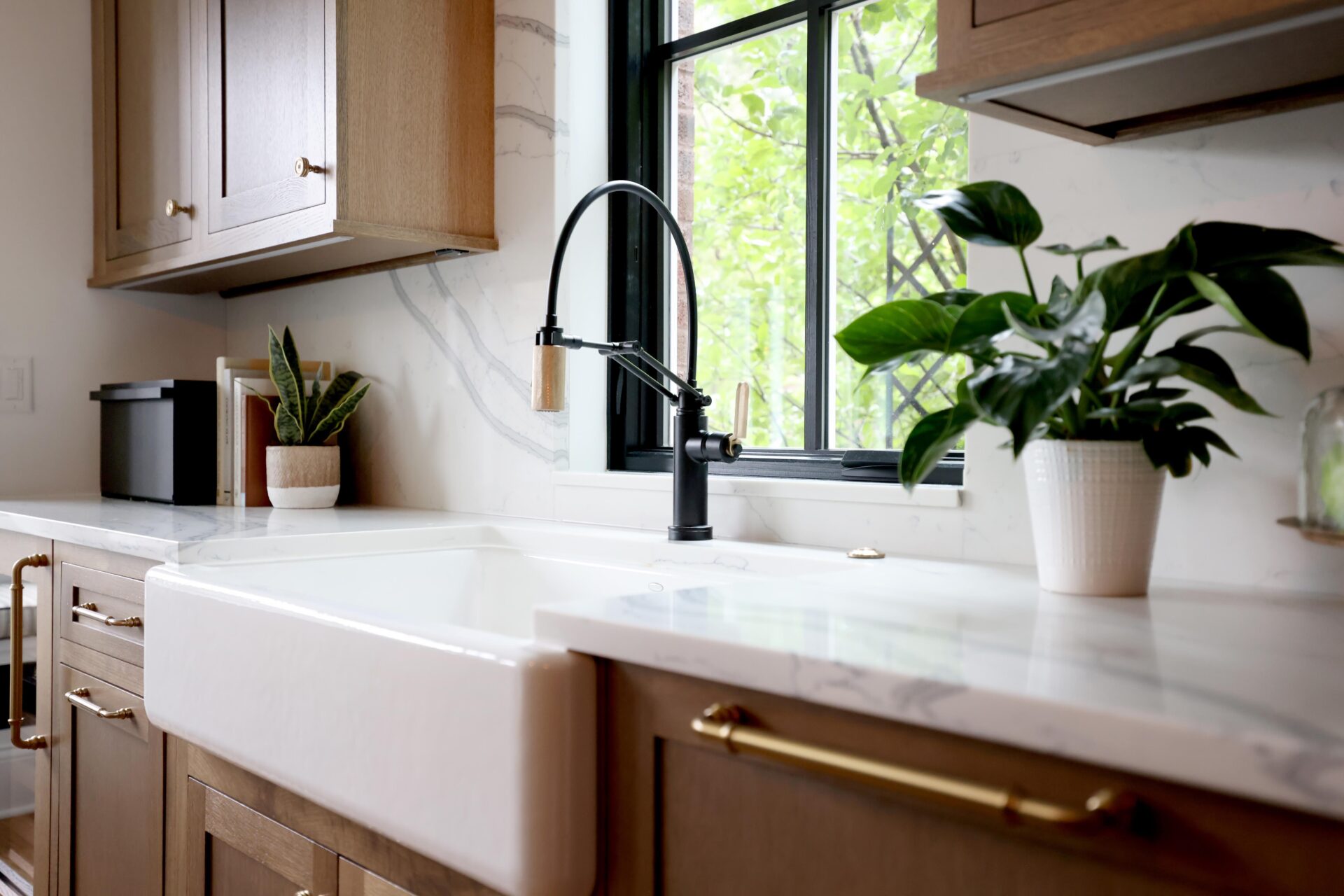 Farmhouse sink with a black and gold faucet in a rift cut white oak kitchen
