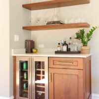 Home dry bar with walnut cabinetry and floating shelves and fridge