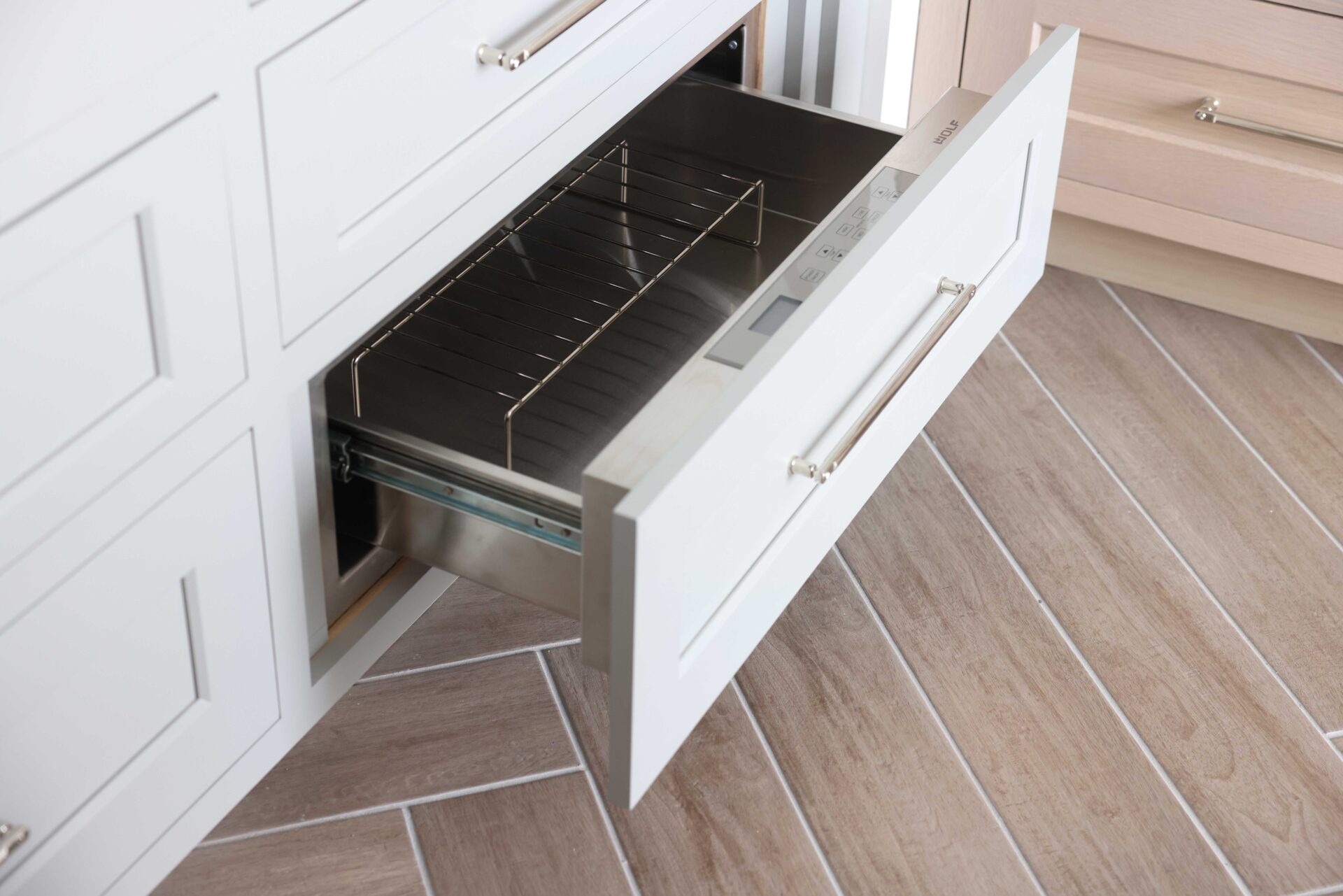 Warming drawer, soft gray cabinetry with polish nickel hardware, porcelain tile floor with wood-grain look