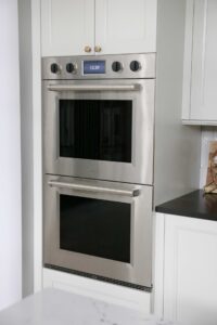 Stacked ovens, stainless steel with black knobs, white cabinet surround