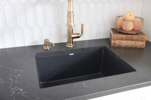 Black sink and countertops with gold faucet, white picket tile backsplash