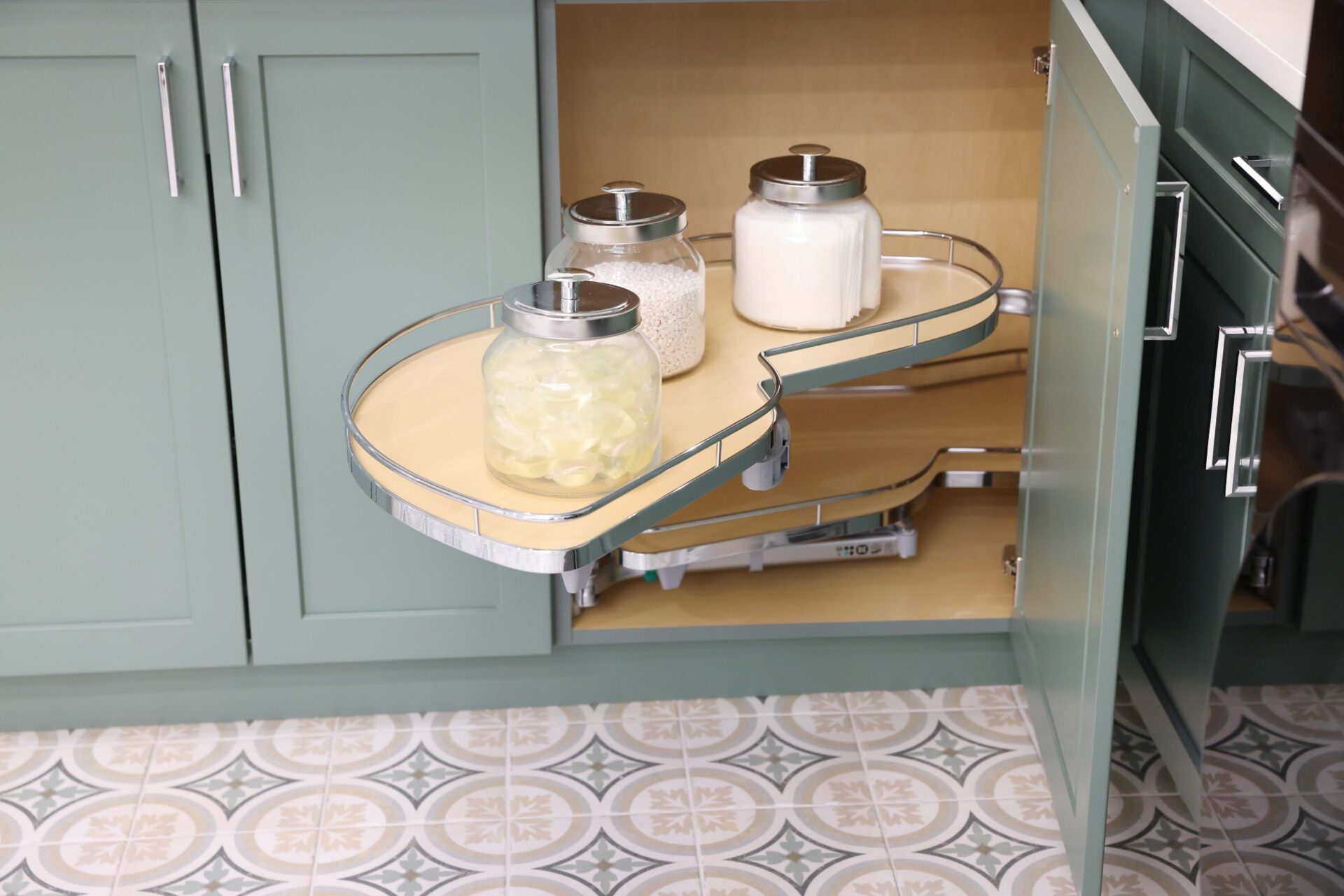 Lazy Susan pull out shelf in laundry room with green cabinets, patterned tile floor, polished chrome hardware