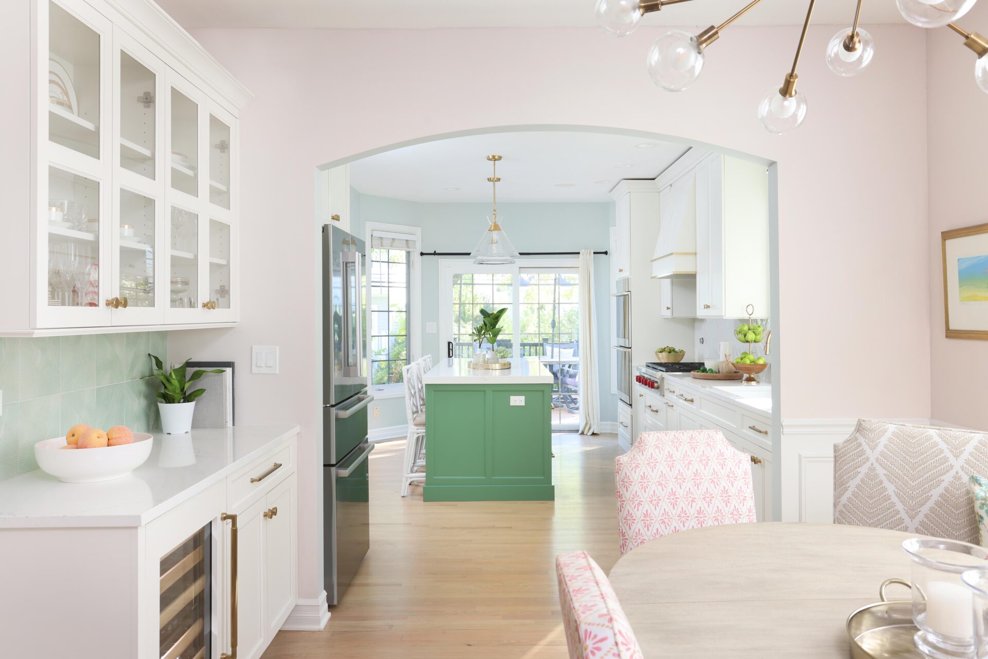 Arched doorway from dining room showing dry bar and framing white kitchen with green island and gold accents