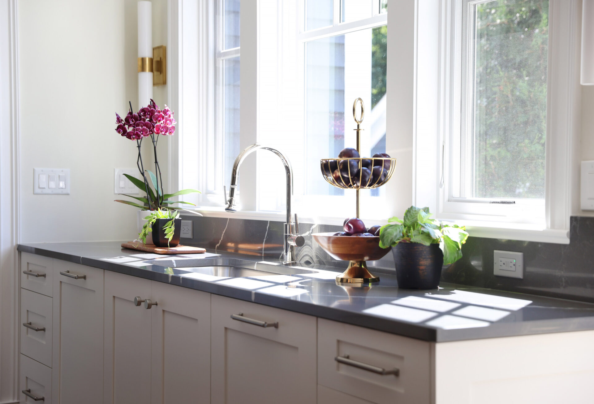White painted cabinets with a dark gray countertop make up this sink wall with windows above