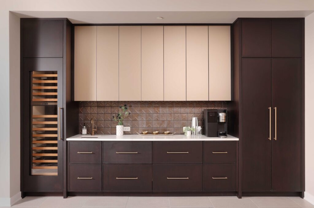 The modern beverage center features rift cut white oak cabinetry, ceramic tile backsplash, quartz countertops, wine fridge, integrated refrigerator drawers, brushed brass elements, and fireclay basin.