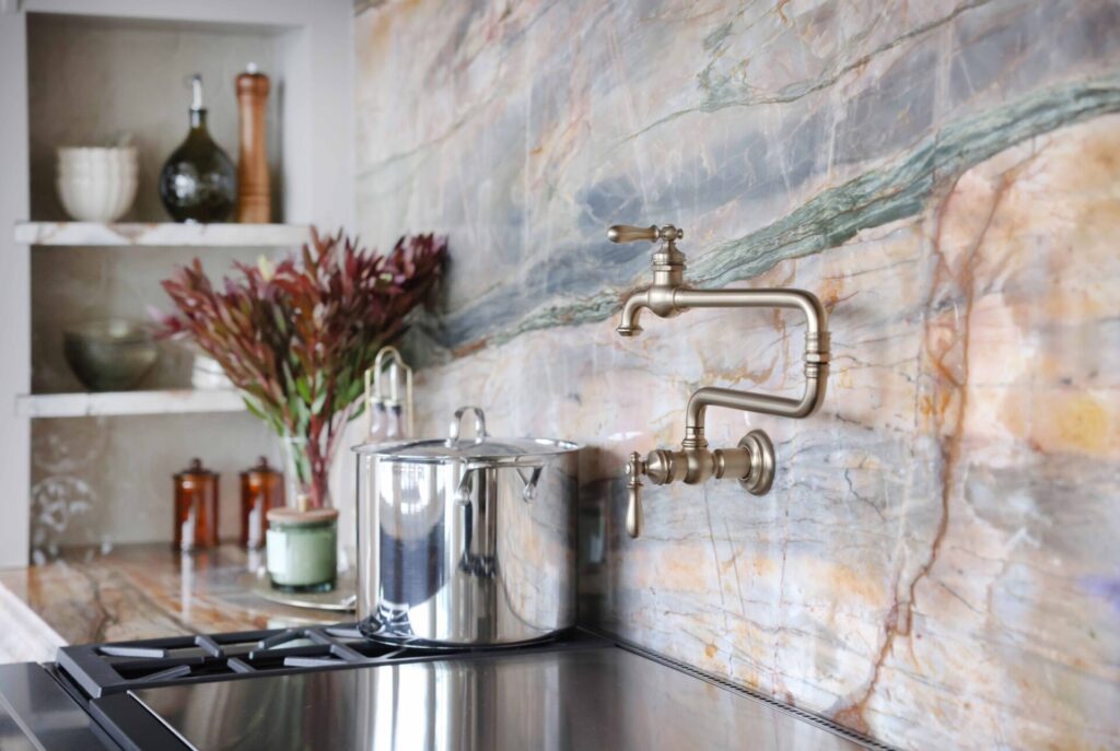 The elevated new traditional kitchen features 48-inch range with Tudor style arched hood. Full height quartzite backsplash with rose and caramel veining. Range area has recessed spice niches; brushed bronze pot filler.