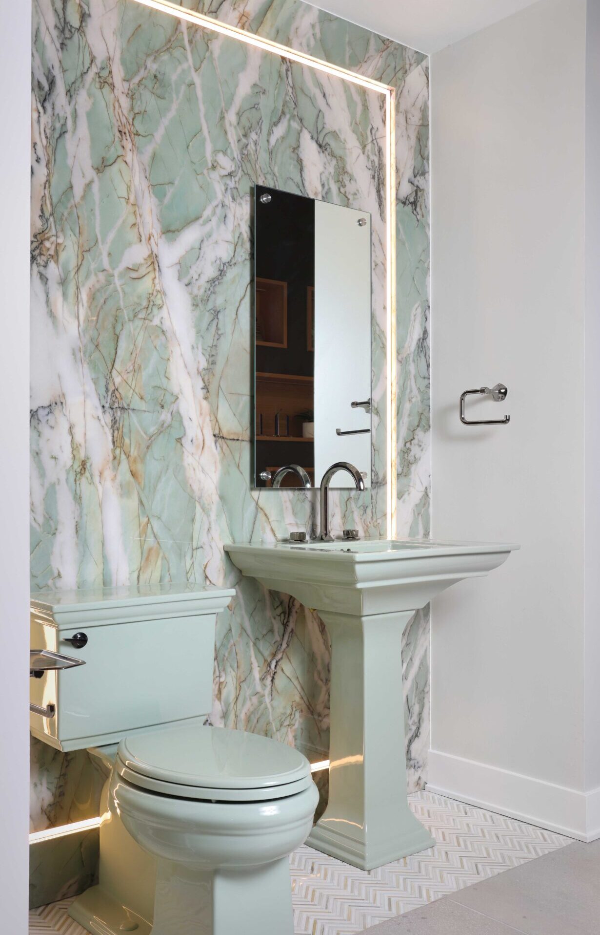The color revival powder room features a richly veined porcelain slab with integrated lighting and floating mirror, aspen green pedestal sink with titanium and black nickel hardware, and marble herringbone floor.