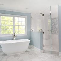 stand alone tub in front of window and shower with half wall and frameless surround