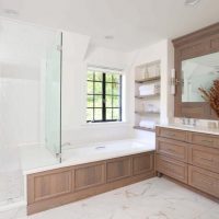 frameless shower attached to deep tub with deck surround in traditional primary bath with oak vanity