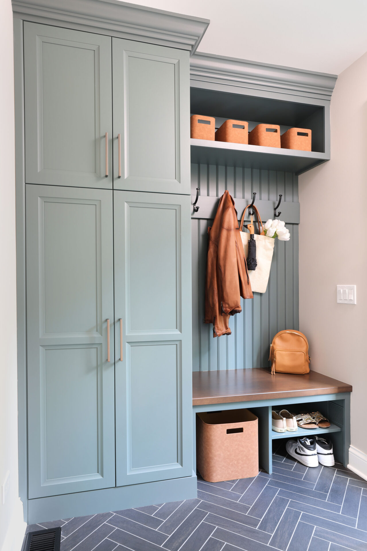 Mudroom with rainforest green cabinets Mudroom with rainforest green cabinets, wood stained mudroom bench with bead board wainscot paneling above, and hooks holding a brown jacket and white bag with umbrella and white flowers. Shelving above and below bench. Lower shelves hold shoes and a brown storage bin. Upper shelf holds four small brown storage bins.