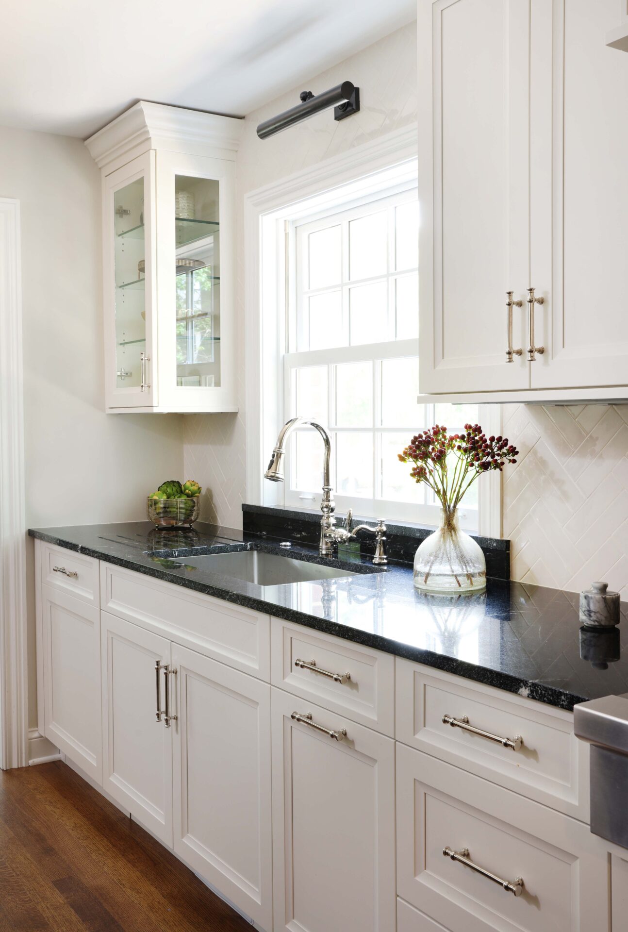 Polished nickel faucet, kitchen sink, white kitchen, black countertops Polished nickel kitchen faucet and cabinet hardware, white kitchen cabinets, black countertops, one upper cabinet glass-fronted cabinet