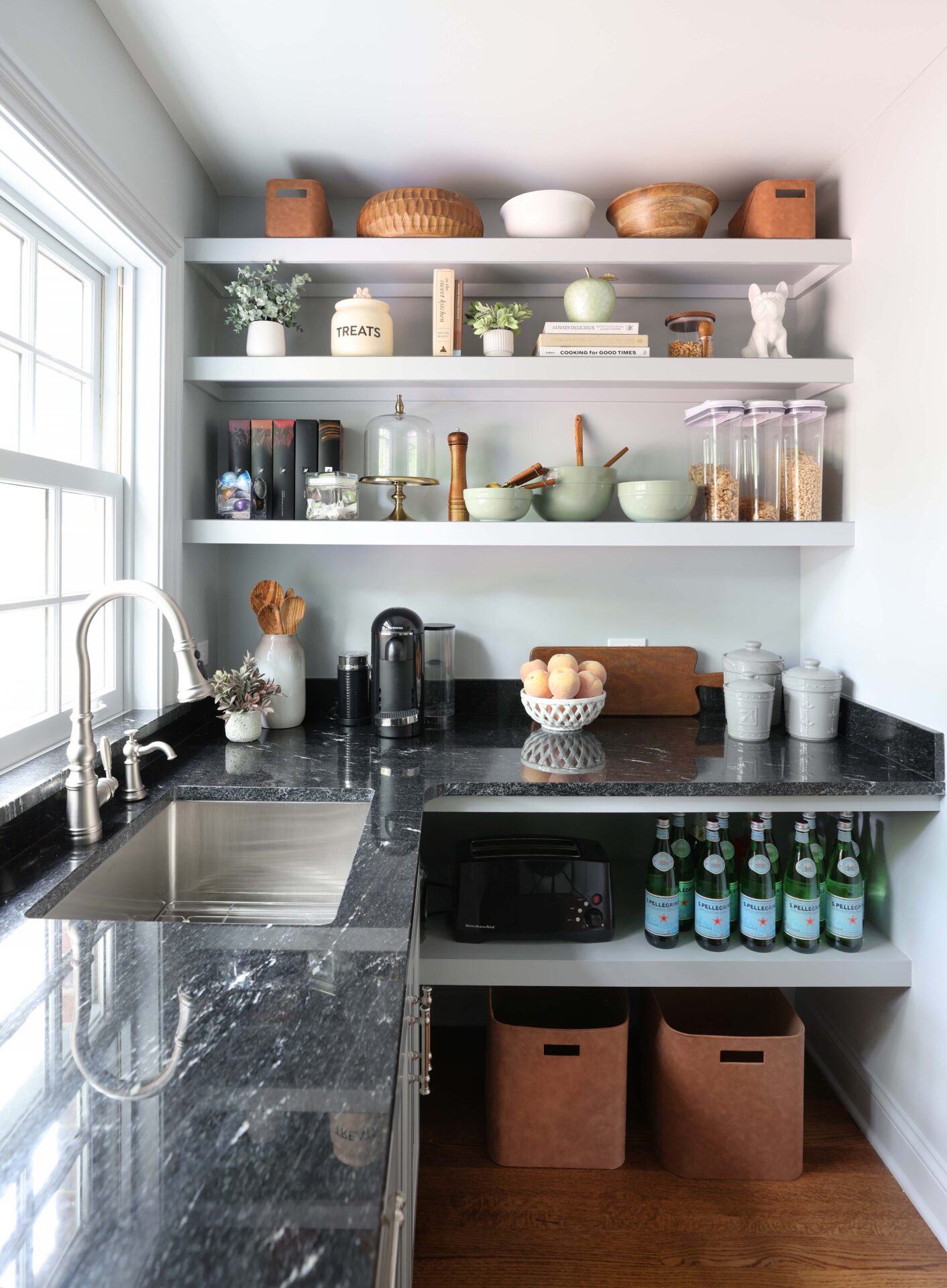 Walk-in pantry with open shelves White kitchen walk-in pantry with sink, polished nickel faucet and black countertops, window above sink