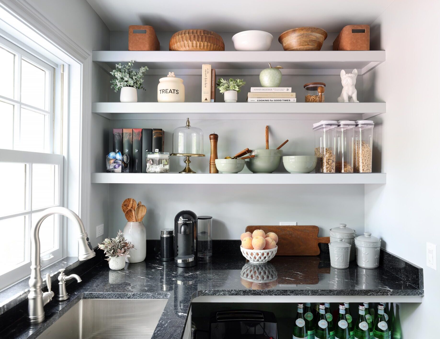 White kitchen pantry with sink, polished nickel faucet and black countertops, window above sink