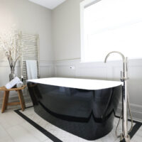 Freestanding tub with black exterior, white interior, polished nickel floor mounted faucet, towel warmer, white and black floor tile